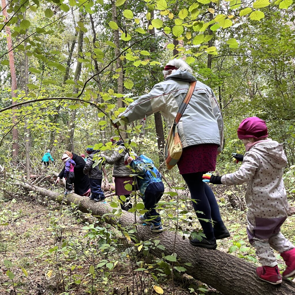 Vaikai su auklėtoja eina miške ant rąsto